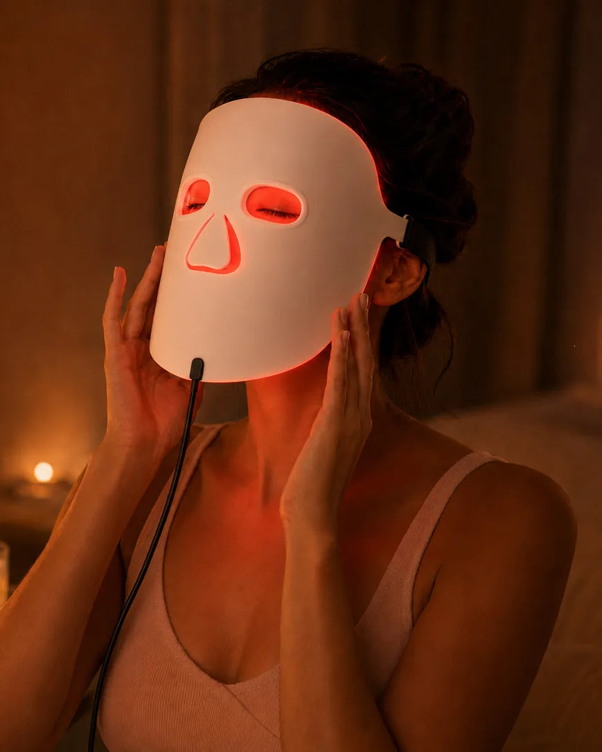 A woman relaxing in soft candlelight wearing The Aura™ LED mask in warm red light.